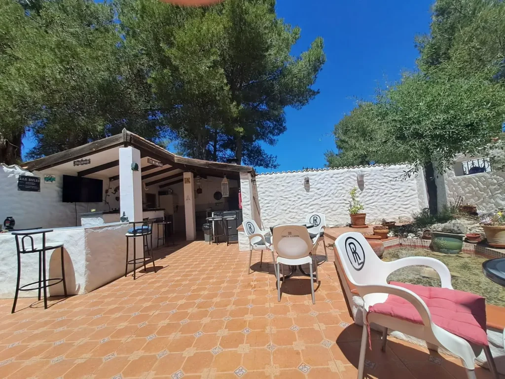 The sunny courtyard with the outdoor kitchen, bar stools and pine trees