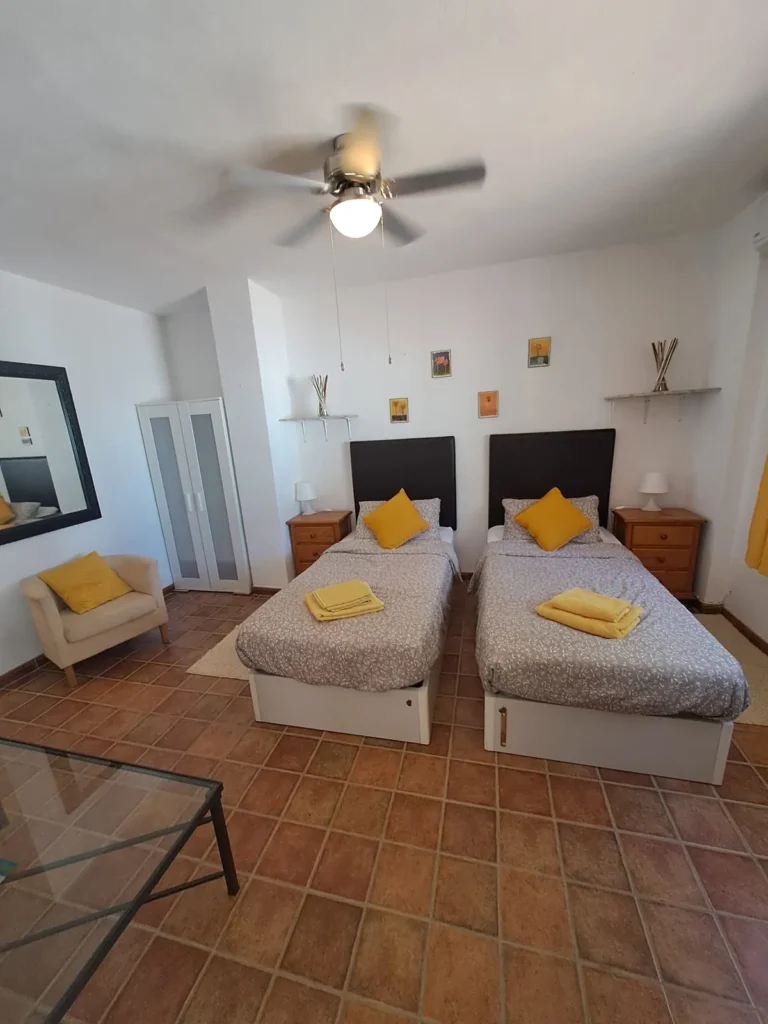 Studio with twin beds, a ceiling fan and yellow accents